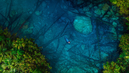 Woman floating on boat in amazing transparent lake with crystal blue water in Indonesia. Aerial view