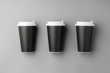 Black disposable cups arranged on a gray surface with white lids, creating a look suitable for a coffee shop setting