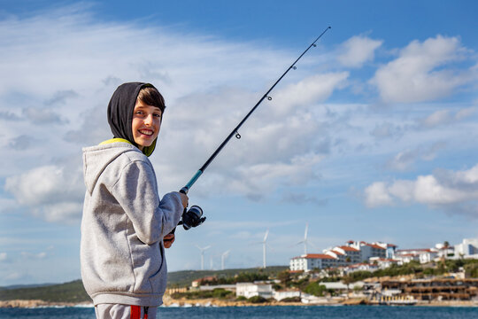 Cheerful boy with fishing rod smiling against blue sky background