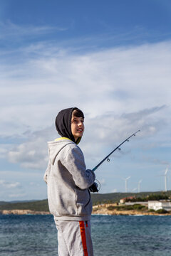 Cheerful boy with fishing rod smiling against blue sky, vertical