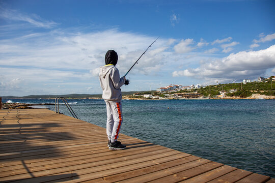 Cheerful boy with fishing rod against blue sky background rear view