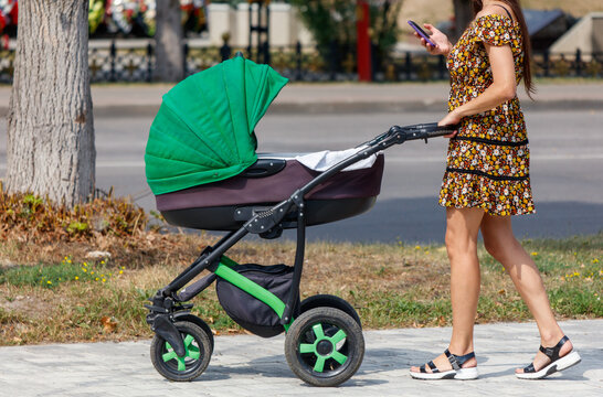 A woman is pushing a stroller with a green canopy