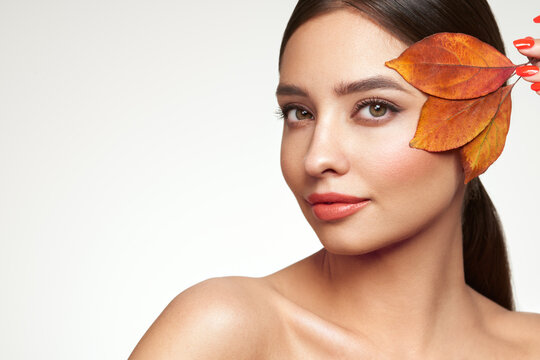 Portrait of beautiful young woman with autumn leafs. Healthy clean fresh skin natural make up beauty eyes and red nails