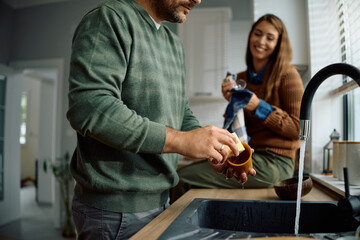 Close up of man washing dishes with his wife in kitchen.