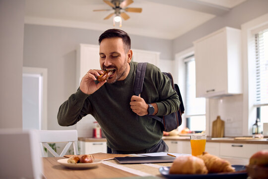 Man in  rush eating sandwich in kitchen.