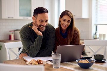 Happy couple using laptop while going through their home budget.