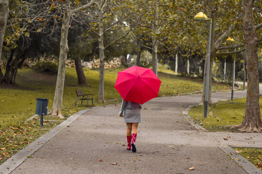 Chica con paraguas rojo caminando bajo la lluvia en un paisaje oto&ntilde;al