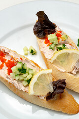 Tasty open-faced sandwiches with tuna spread, topped with fresh vegetables and lemon slices on a white plate