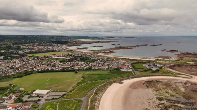 Guernsey Grandes Rocque and Cobo Bay high drone flight approaching the bay with views across golden beach and out to sea under interesting cloudy sky