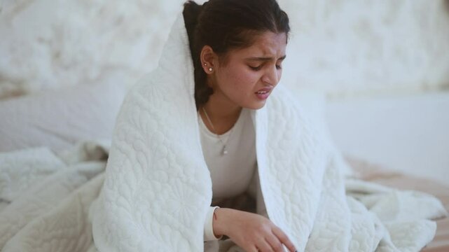 Portrait of crying young indian woman with smartphone sitting on bed under the blanket and reading bad news email break up message from ex-boyfriend or personal problems at home bedroom