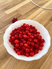 Collection of vibrant red berries sits elegantly in a white bowl, creating a striking contrast against a wooden background. Simple composition showcases the freshness and natural appeal of the fruit