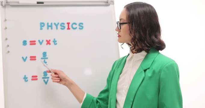 Woman physics teacher explains formula for calculating mass on white background. Pedagogue stands by whiteboard and explains formulas at lesson