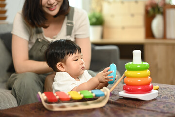 Obraz premium Loving young mother and cute toddler boy playing with educational didactic toy in living room