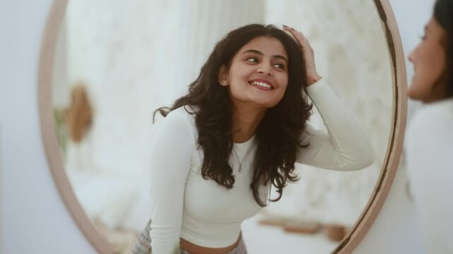Portrait of pretty dark haired indian woman looking at mirror reflection and doing self hair scalp massage with massager at home Concept of hair loss growth stimulation trichology self care	