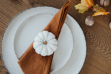 Elegant autumn table setting featuring a decorative white pumpkin and warm orange napkin
