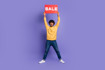 Photo of confident positive man wear stylish yellow clothes arms hold red billboard sale news isolated on purple color background
