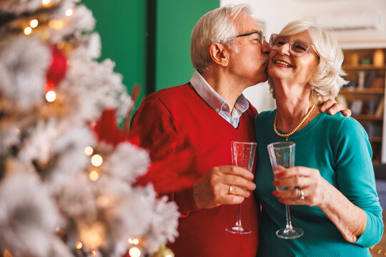 Senior couple kissing and drinking champagne by the Christmas tree