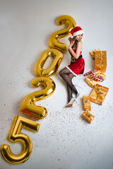 Miss Santa Claus lies on a white background surrounded by gifts and the inscription 2025, top view