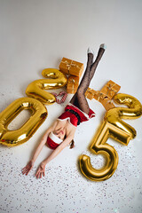 Miss Santa Claus lies on a white background surrounded by gifts and the inscription 2025, top view