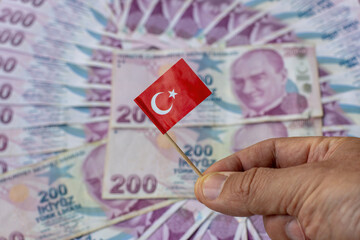 Turkey’s 200 lira banknotes spread out, hand holding Turkish Flag in focus, illustrating the...