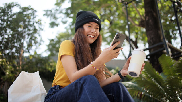 Gen Z eco go green woman asia sit happy relax at tree public park city life enjoy typing mobile phone drink coffee bottle use reuse tote bag care save the earth planet net zero waste clean future hope
