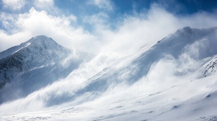A strong wind whips snow off a mountain peak, creating a swirling cloud of white against a blue sky.