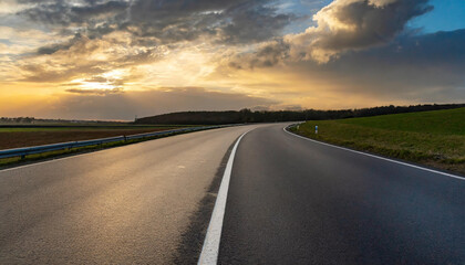 Naklejka premium Scenic winding road under a dramatic sky at sunset in the countryside