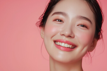 Obraz premium A close-up of a young woman smiling radiantly against a soft pink background, showcasing smooth, glowing skin, natural makeup, and a joyful expression