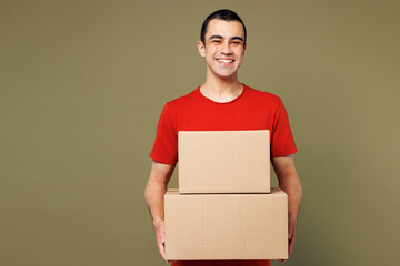 Young smiling happy cheerful middle eastern man wear red t-shirt casual clothes hold stack of cardboard boxes look camera isolated on plain pastel green background studio portrait. Lifestyle concept.