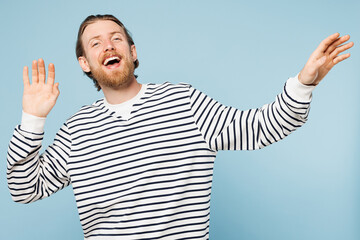 Naklejka premium Young smiling happy overjoyed man he wear striped sweatshirt casual clothes dancing raise up hands look camera isolated on plain pastel light blue cyan background studio portrait. Lifestyle concept.