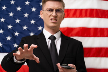 Greedy business Man in a suit is a stack of money. He is standing in front of an American flag....