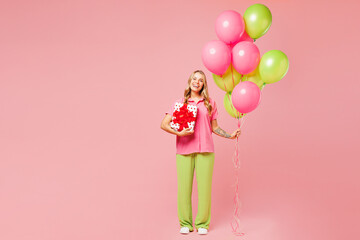 Full body young woman wear shirt celebrating birthday holiday and hold bunch of colorful air balloons hold present box with gift ribbon bow isolated on plain light pink background. Lifestyle concept.