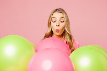 Naklejka premium Close up young shocked surprised excited astonished fun woman celebrating birthday holiday looking at bunch of colorful air balloons isolated on plain pastel light pink background. Lifestyle concept.