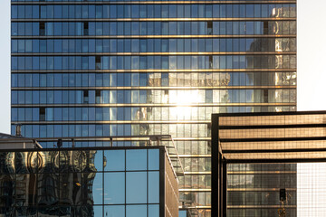 An office building encased in glass reflects sunlight in an urban setting. The interplay of reflections creates a dynamic, visually appealing urban skyline.