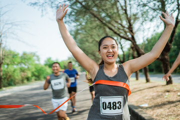 woman marathon runner crossing finish line with hands up gesture