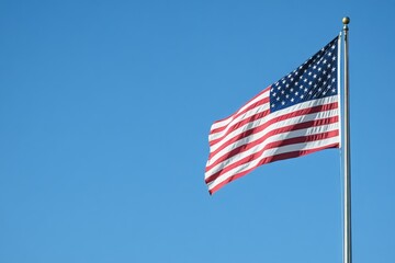 Fototapeta premium An American flag gently waving against a clear blue sky in the afternoon sunshine