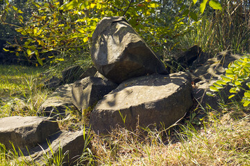 Natural still life with large angular stones irradiated by the sun's rays. Large square stones placed under a tree. Nature, tree, grass, stones, sunny day.