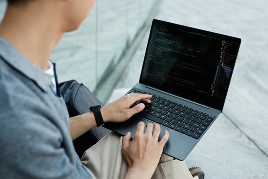 Close up on hands of unrecognizable male IT programmer typing on laptop keyboard writing code while sitting outside in city street, copy space