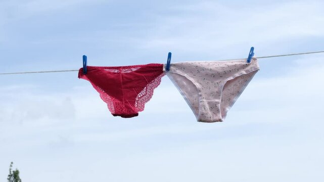 pair of pink cotton panties and red lace panties hang side by side on a clothesline under a clear sky. This image highlights the contrast between soft, breathable cotton and delicate, decorative lace