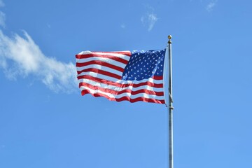 Obraz premium The American flag flutters gracefully in the wind, showcasing its vibrant colors against a bright blue sky, representing the spirit of the nation.