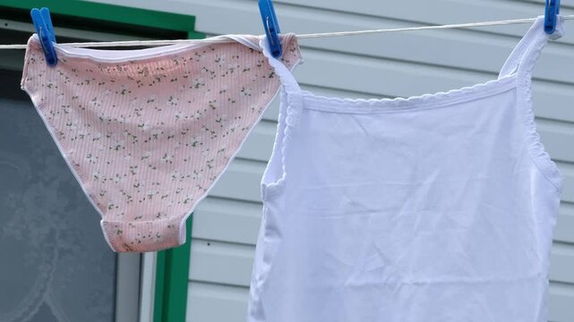 A person is hanging clean underwear and a tank top on a clothesline. The image captures the concept of fresh air drying and home comfort.