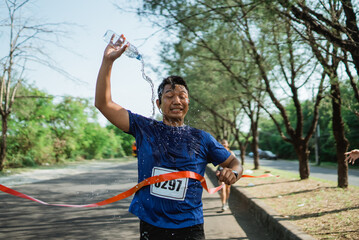 asian runner in sportswear crossing finish line with pouring water onto his body