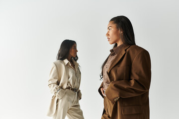 Two young and fashionable women pose confidently in stylish attire against a simple backdrop.