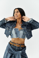 A fashionable young woman adjusts her stylish denim outfit while posing gracefully indoors.