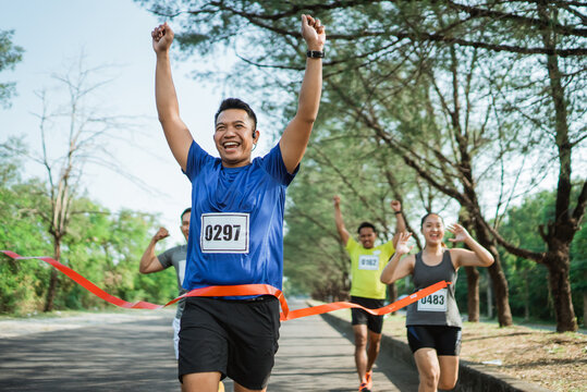 asian marathon participant crossing finish line with hands up gesture