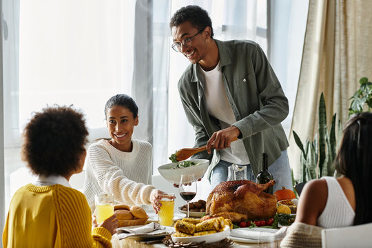 A group of friends gathers at home, sharing laughter and delicious food during Thanksgiving.
