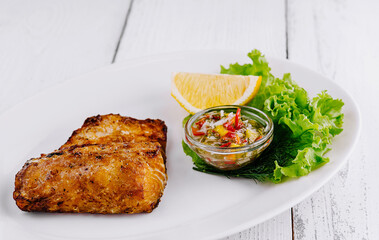Grilled salmon fillet served on white plate with lemon and sauce