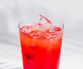 Red cocktail standing on white cube with palm leaf shadow
