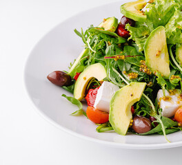 Fresh salad with avocado, feta cheese and olives served on white plate
