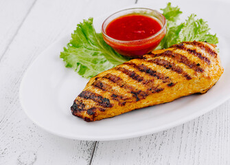 Grilled chicken breast served with lettuce and sauce on white plate